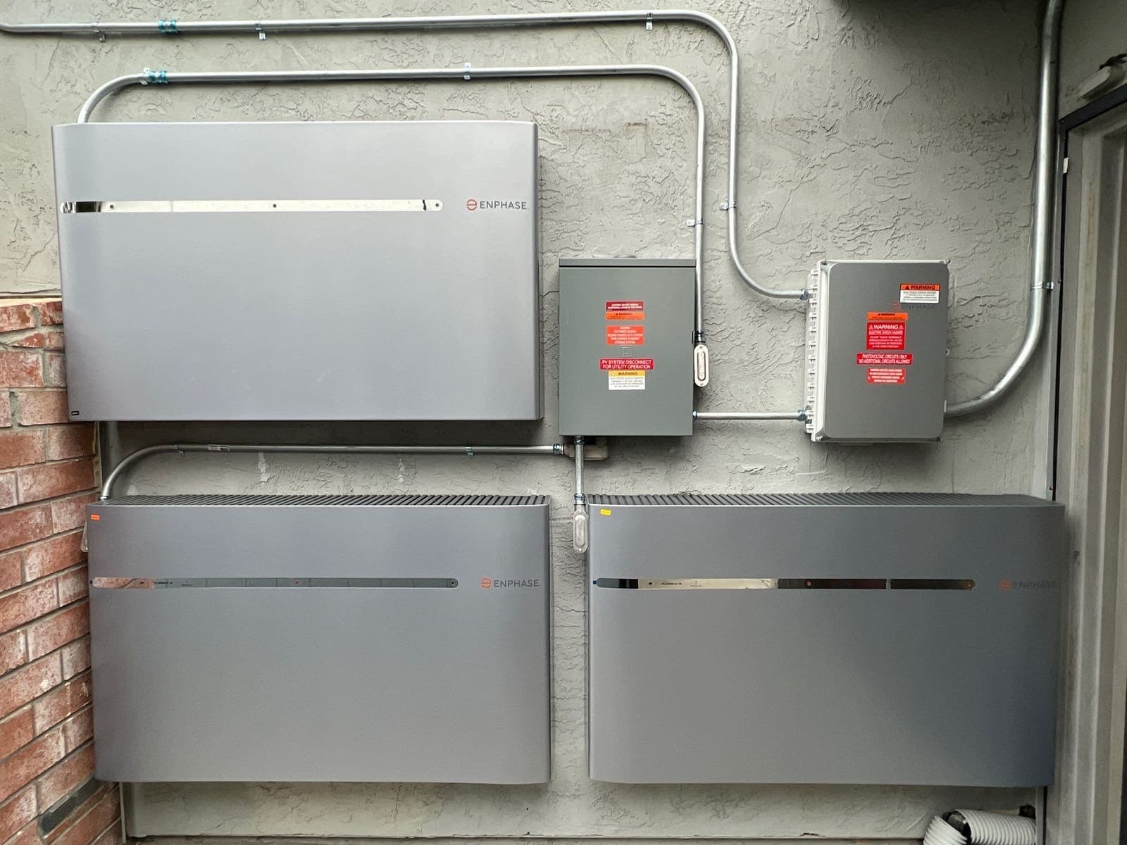 Three home battery units mounted on an exterior wall with conduit runs between them