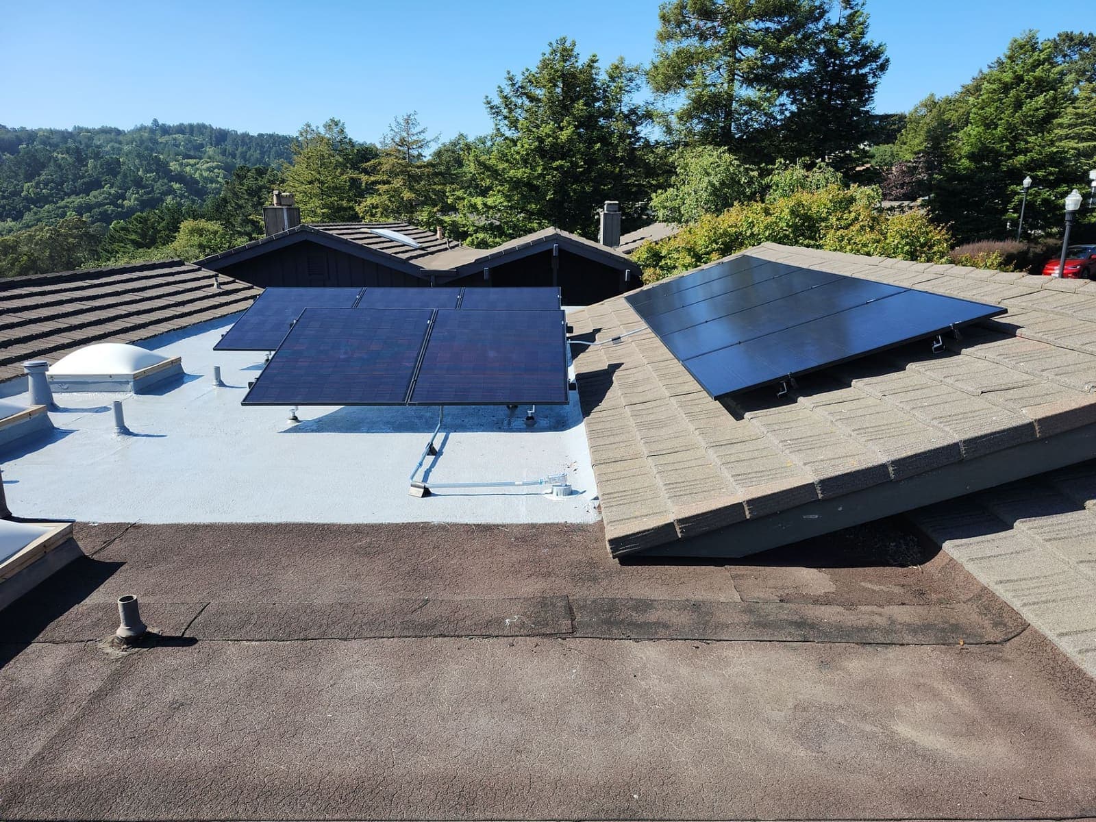Tilt-mounted solar panels on a low-slope roof with hills behind